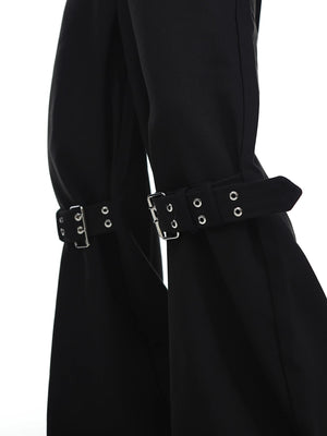 Close-up of industrial buckle and strap details on black punk-style trousers.