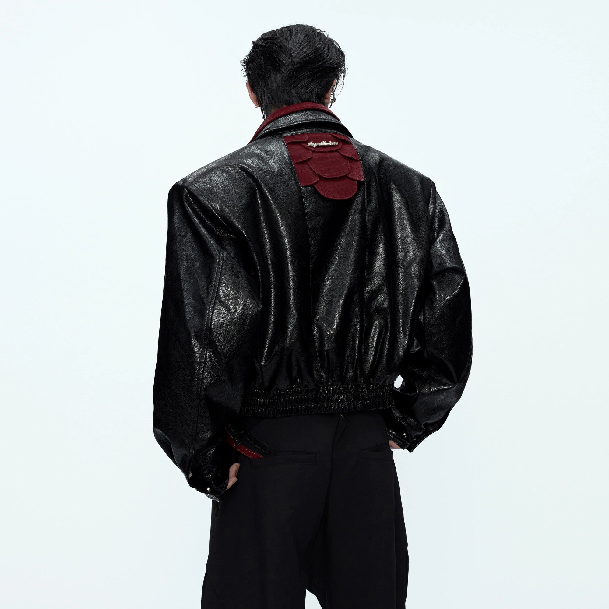 Front view of a glossy snakeskin patchwork moto jacket in black