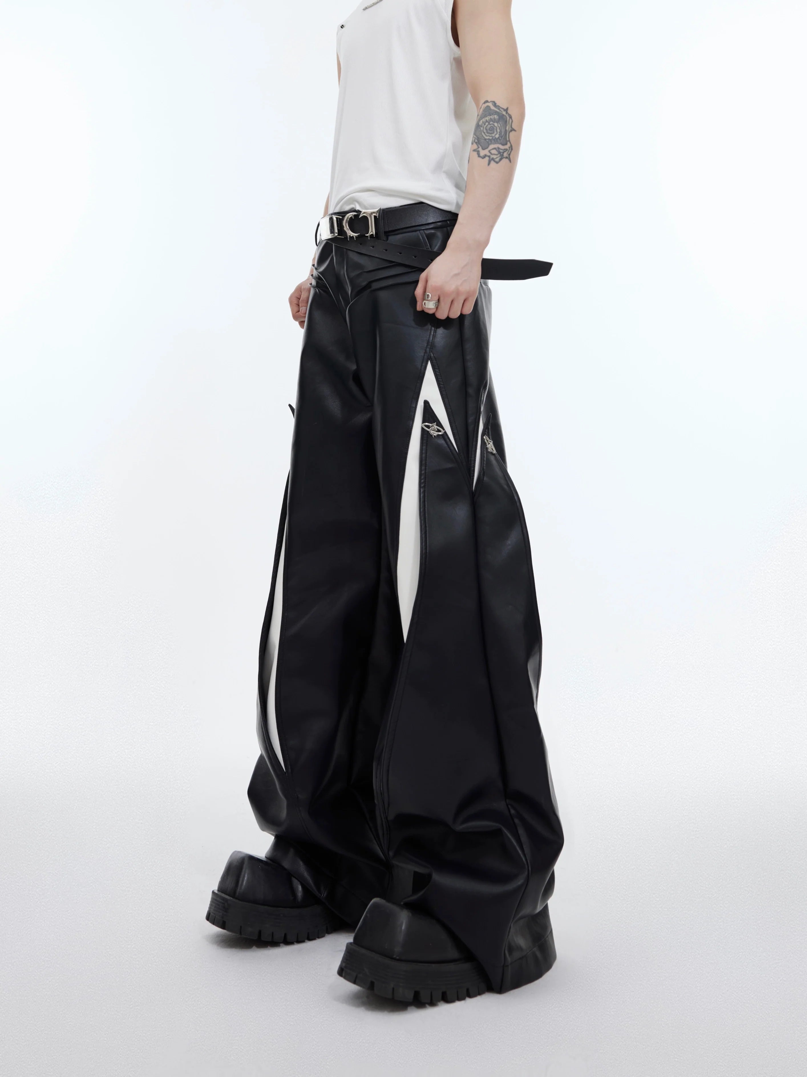 Front view of deconstructed leather pants with metal buttons, showcasing wide leg streetwear design and asymmetric patchwork details