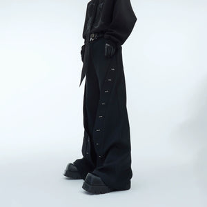 Front view of wide-leg trousers with metal trim detailing, showcasing the loose drop-crotch streetwear style