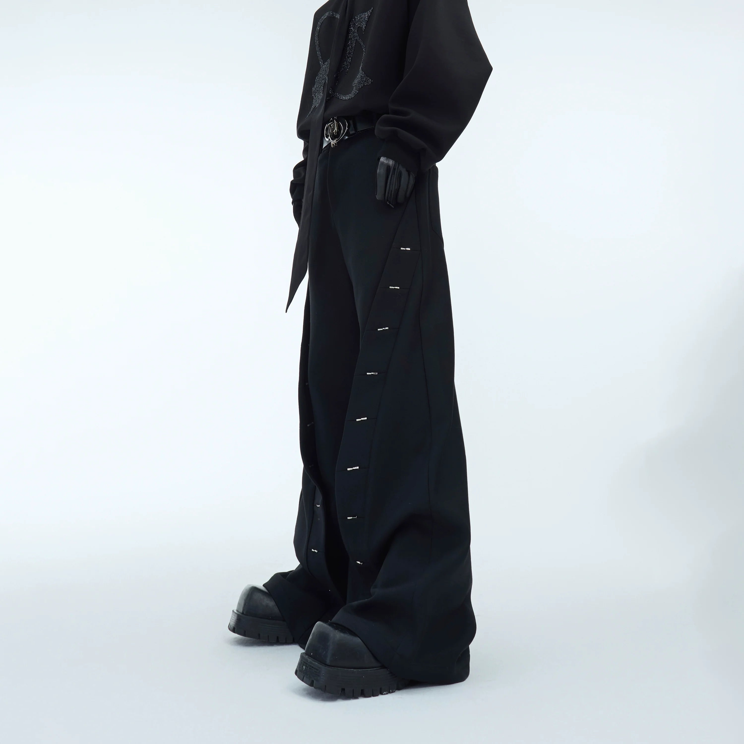 Front view of wide-leg trousers with metal trim detailing, showcasing the loose drop-crotch streetwear style