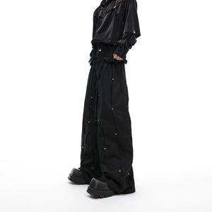 Front view of deconstructed pleated cargo pants with metal studs, showcasing the stacked loose fit and distressed details