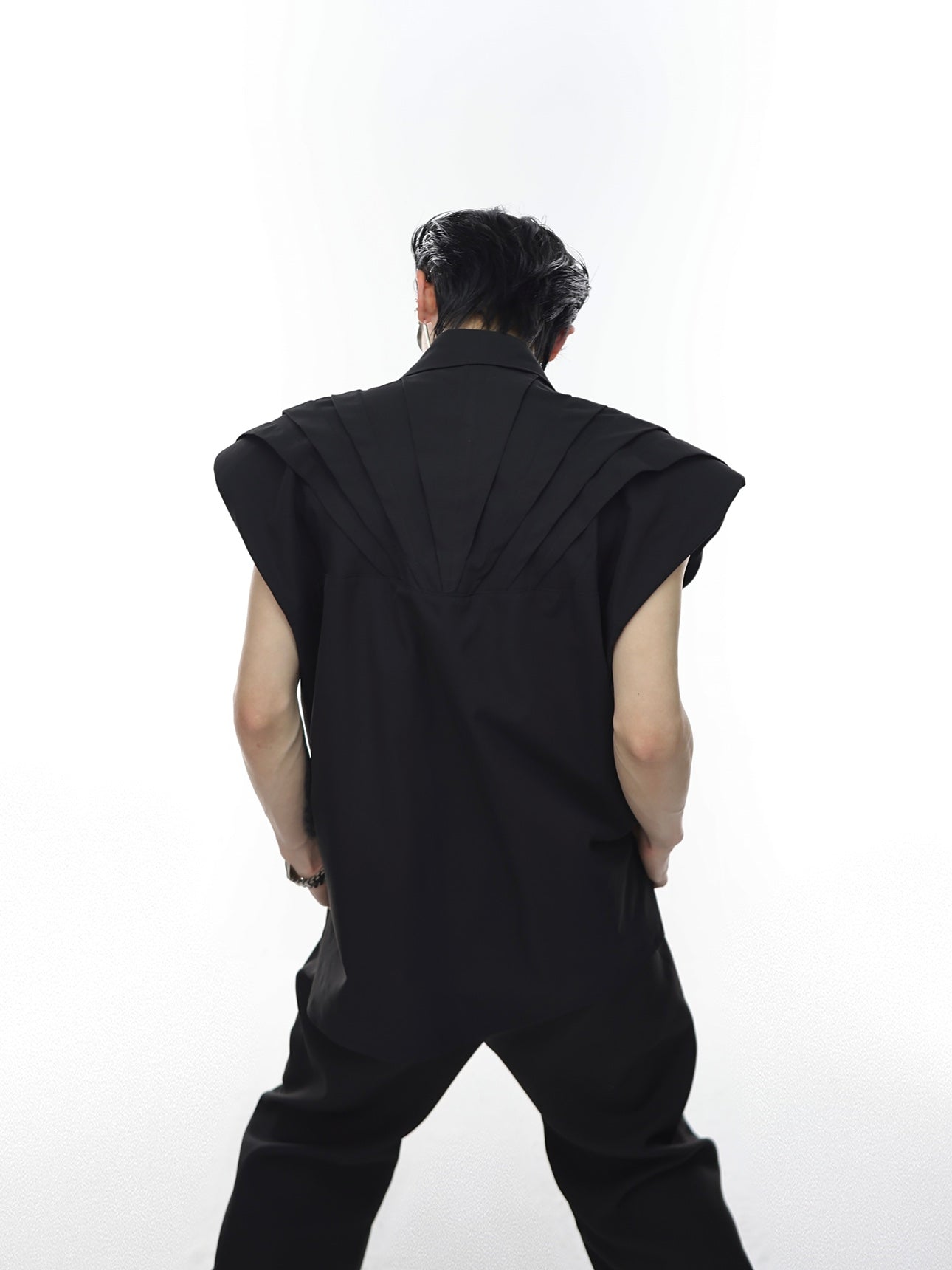 Back angle showing architectural tailoring of deconstructed vest with structured shoulder pads for dramatic silhouette