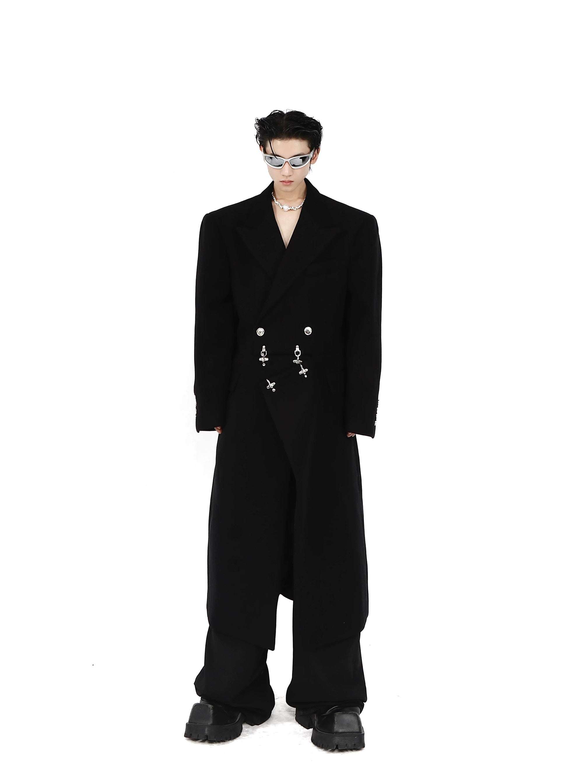 Model wearing a black deconstructed wool coat with metal buckles in a street setting