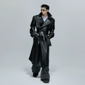 Model wearing a long black leather trench coat in an urban street setting