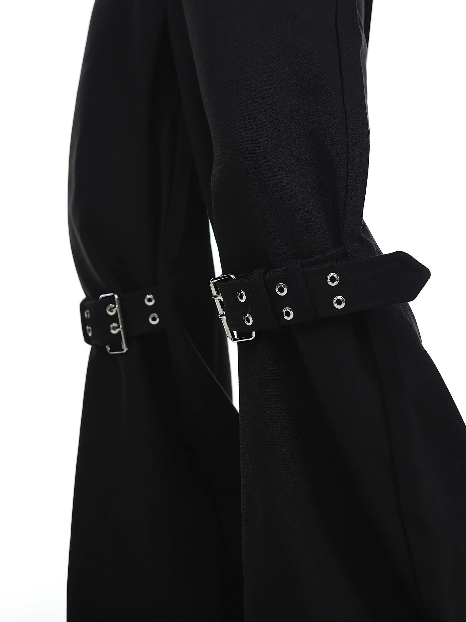 Close-up of industrial buckle and strap details on black punk-style trousers.