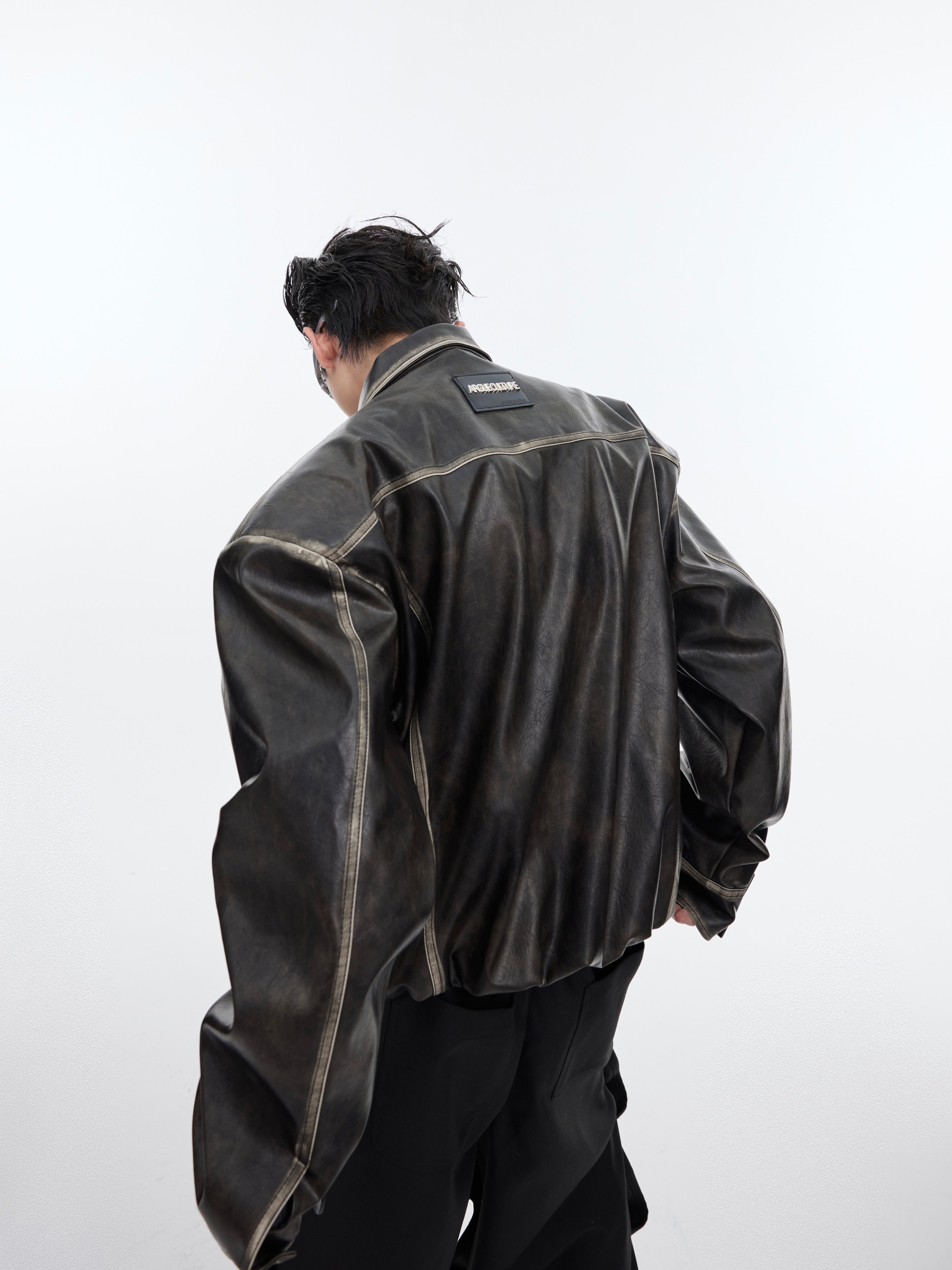 Close-up of distressed leather texture on oversized cropped biker jacket with geometric split panel design