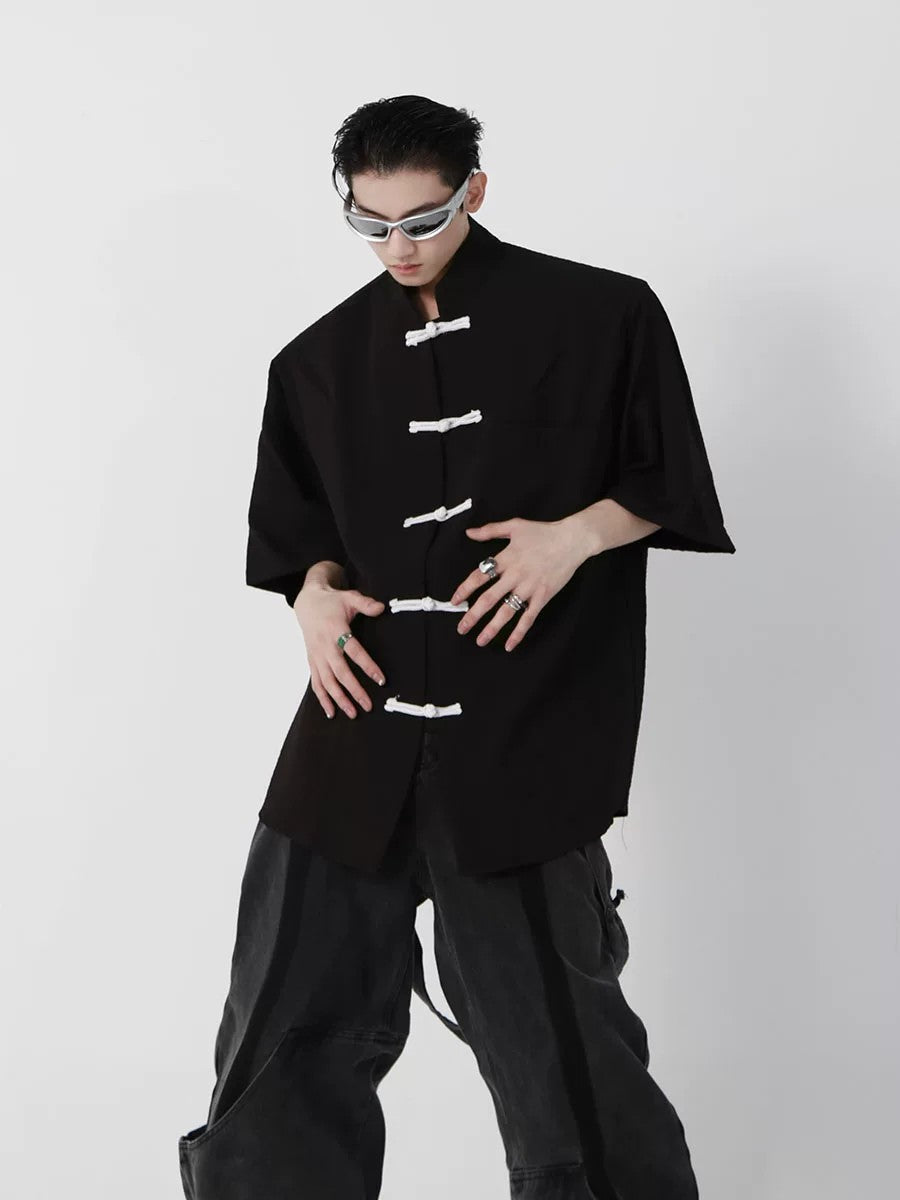 Front view of black streetwear tee with padded shoulders and frog buttons