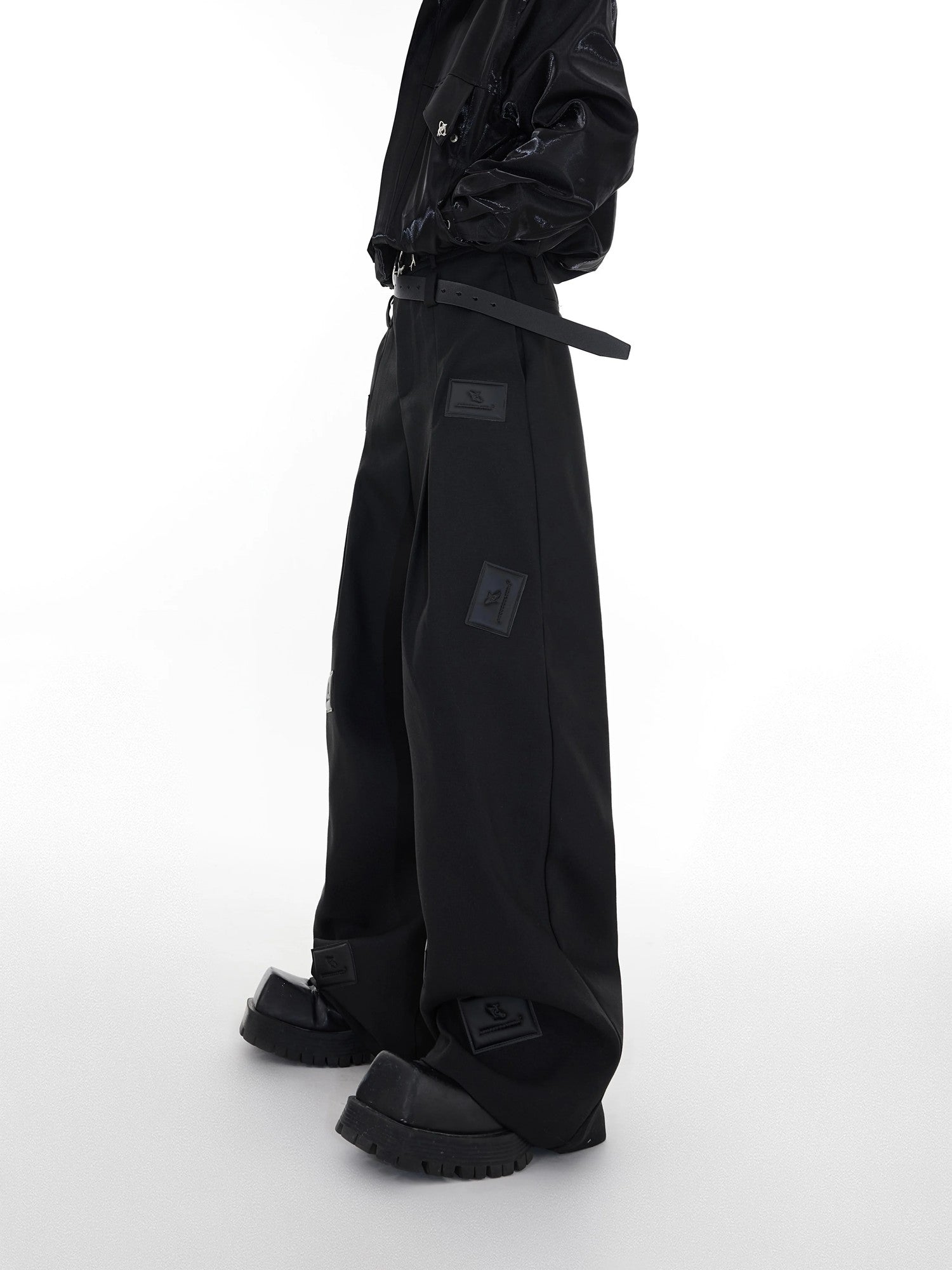 Front view of black wide-leg streetwear suit pants with 3D leather patches
